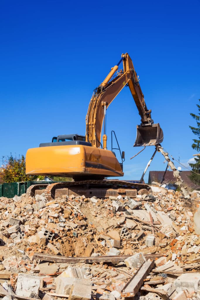 Démolition de bâtiment: Pelle mécanique sur gravats sous ciel bleu Pelle mécanique orange sur un tas de gravats, démolissant activement une structure sous un ciel bleu clair. Démolition de bâtiment.